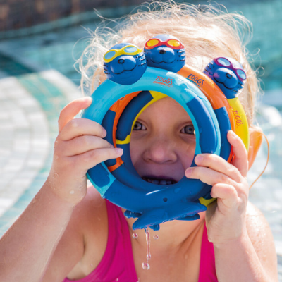 little girls sitting in the pool holding dive rings up to her face to look through them 
