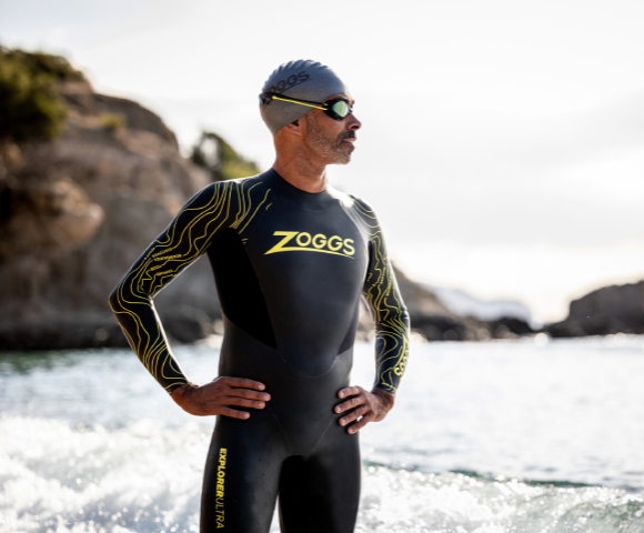 Man is swimming in the open water and wears a goggle and a cap of zoggs