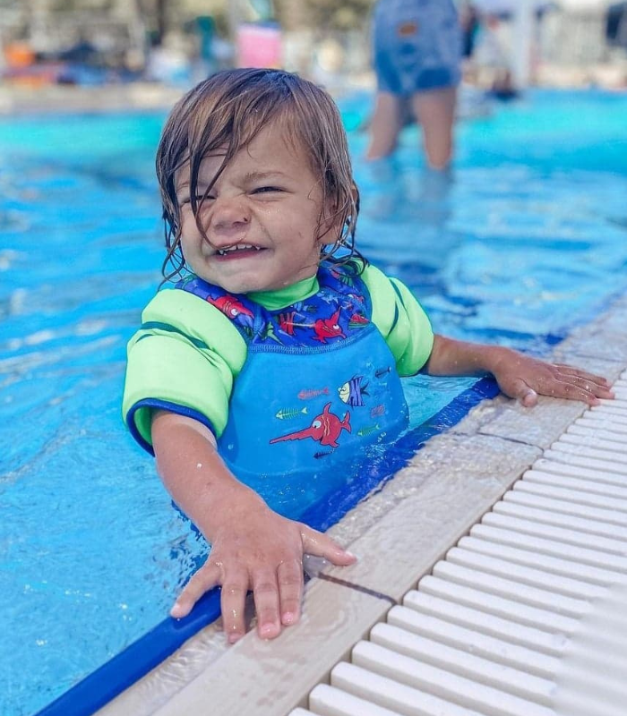 Boy in pool smiling in a water wings floatsuit