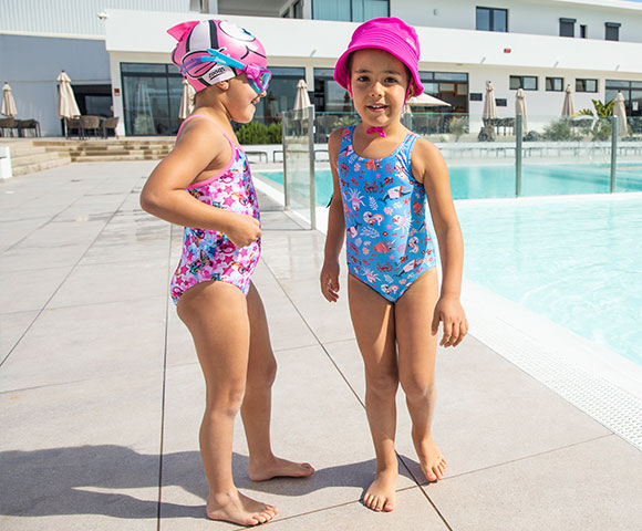 Two girls wearing blue/pink flowered swimsuits and goggles