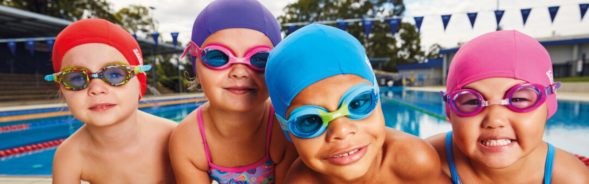 4 kids next to the pool in kids goggles and swim caps 