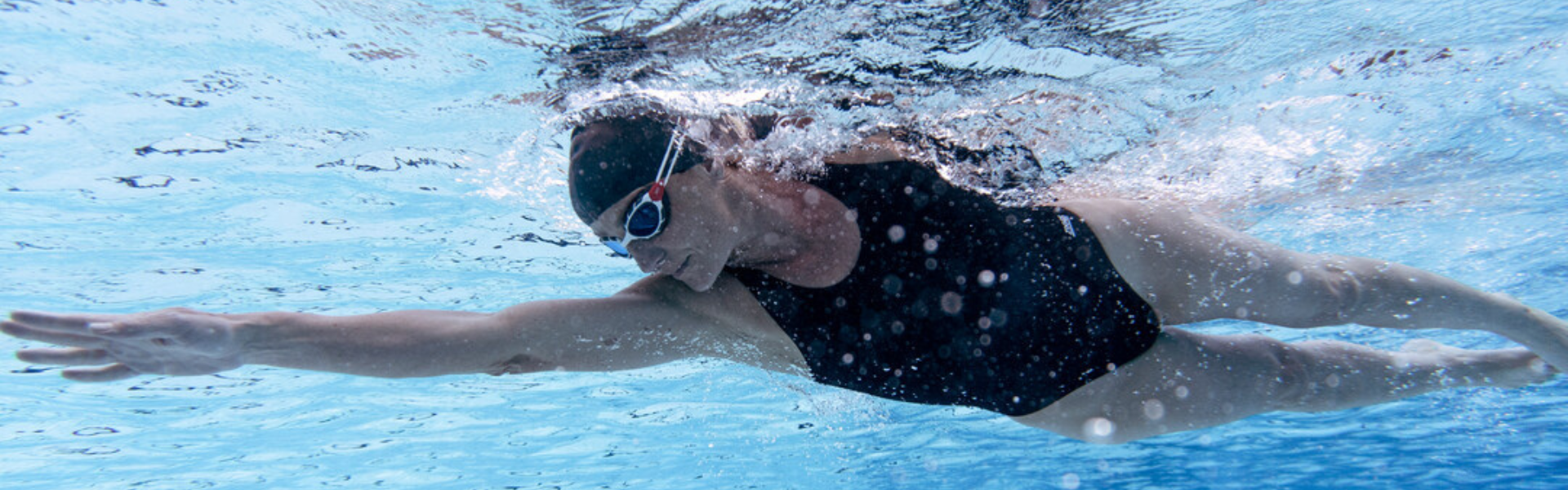 woman swimming under water in black one piece and predator goggles  