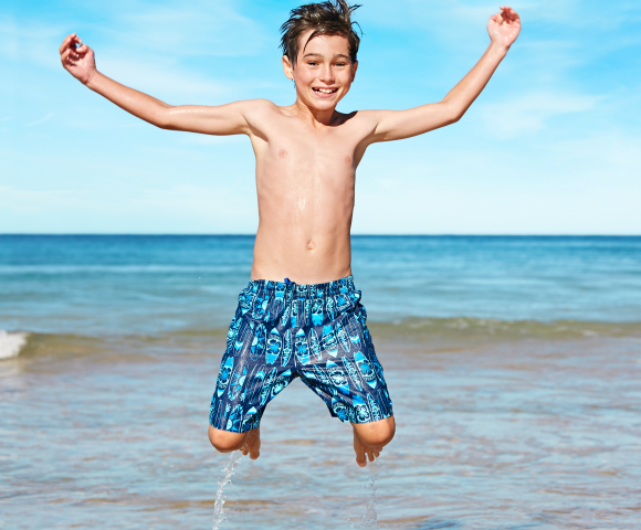 Boy wears a blue swim short and is jumping