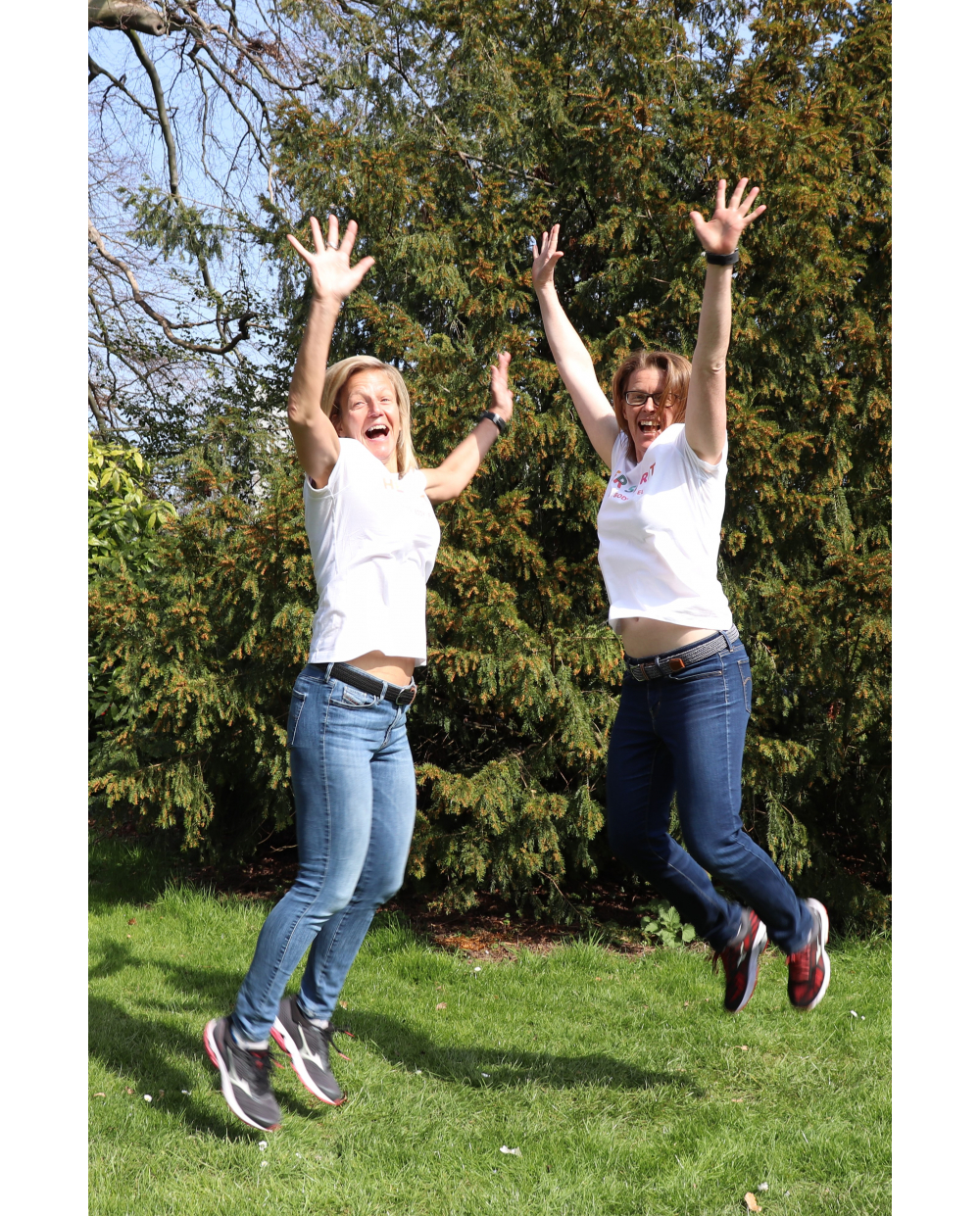 Two womens wearing white t-shirts and jeans are jumping